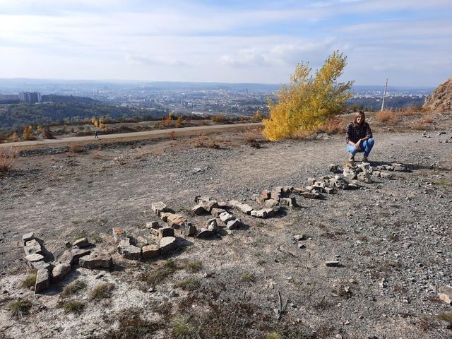 Amelie hockt neben einem Striftzug aus Steinen auf einem Berg.