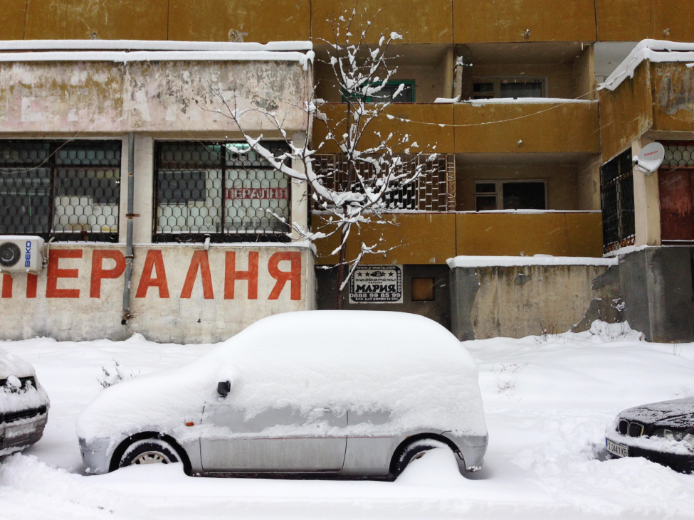 Bild eines zugeschneiten Autos vor einer Häuserfassade in Sofia