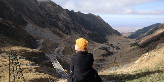 Freiwillige Angelique sitzt mit Mantel und Mütze in einer hügeligen Landschaft